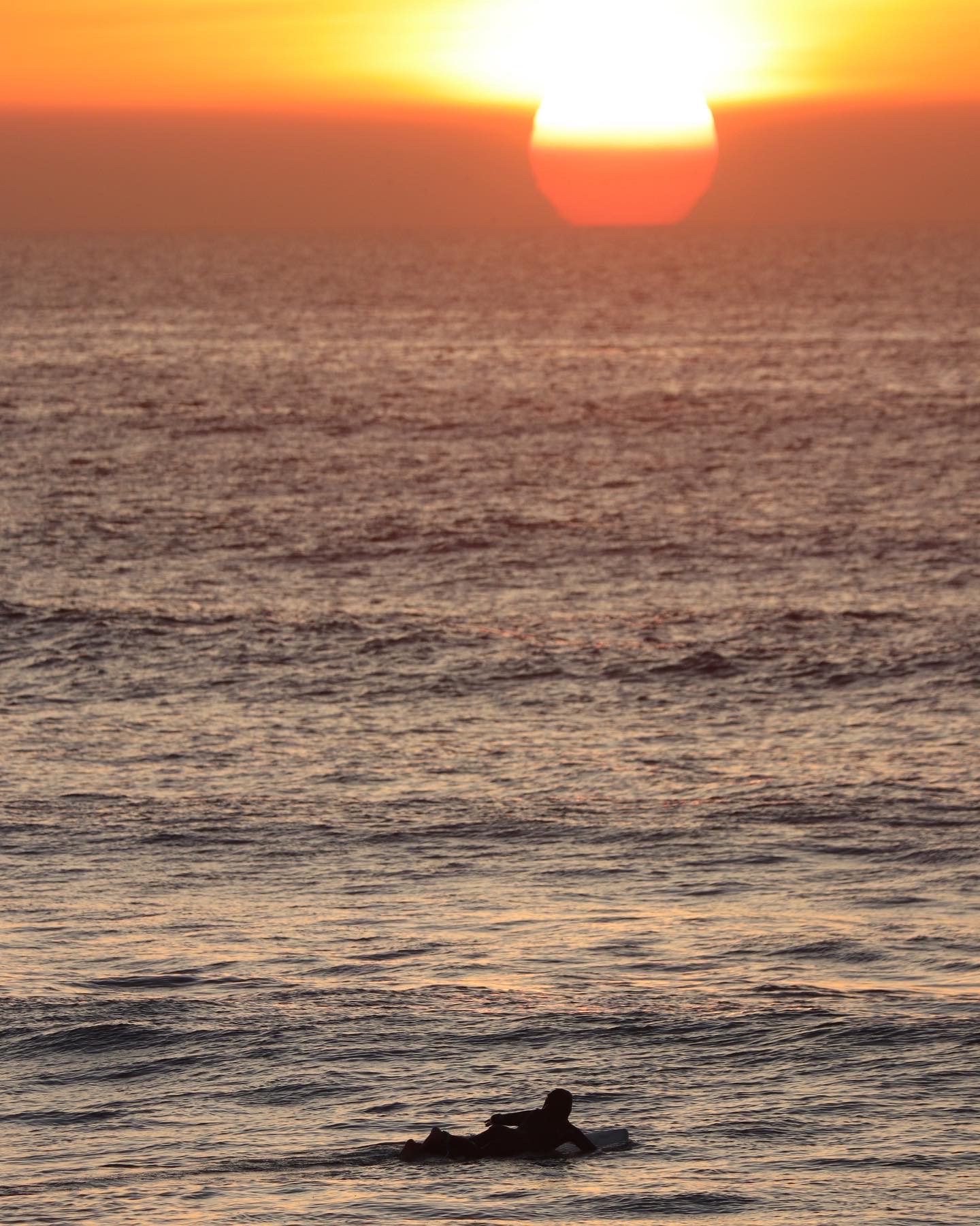A surfer paddling out toward the sunset